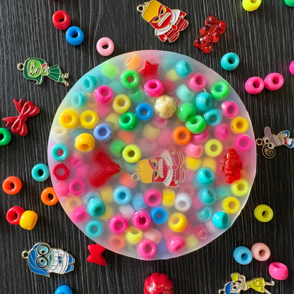 Colorful beads in a transparent container on a dark surface with various small toys around.